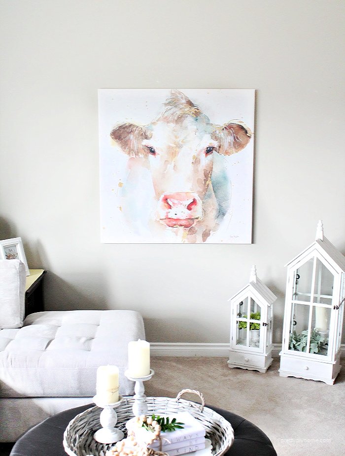 A living room wall decorated with a watercolor farmhouse cow canvas print in pretty pastel colours.