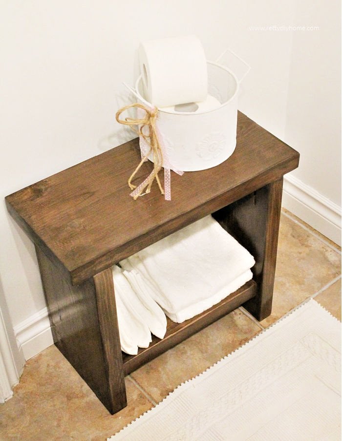 A modern farmhouse DIY milky brown bench with white towels and white farmhouse container holding white toilet paper.