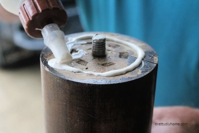 Using wood glue to attach a wood plaque to the bottom of a wood table leg while making DIY candle holders.