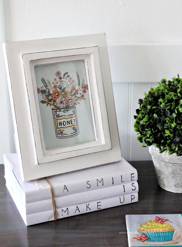 A farmhouse vignette with a free farmhouse printable in a frame, some moss and a farmhouse book stack.