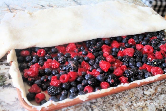 Placing the top layer of pie crust on a bumbleberry slab pie recipe.