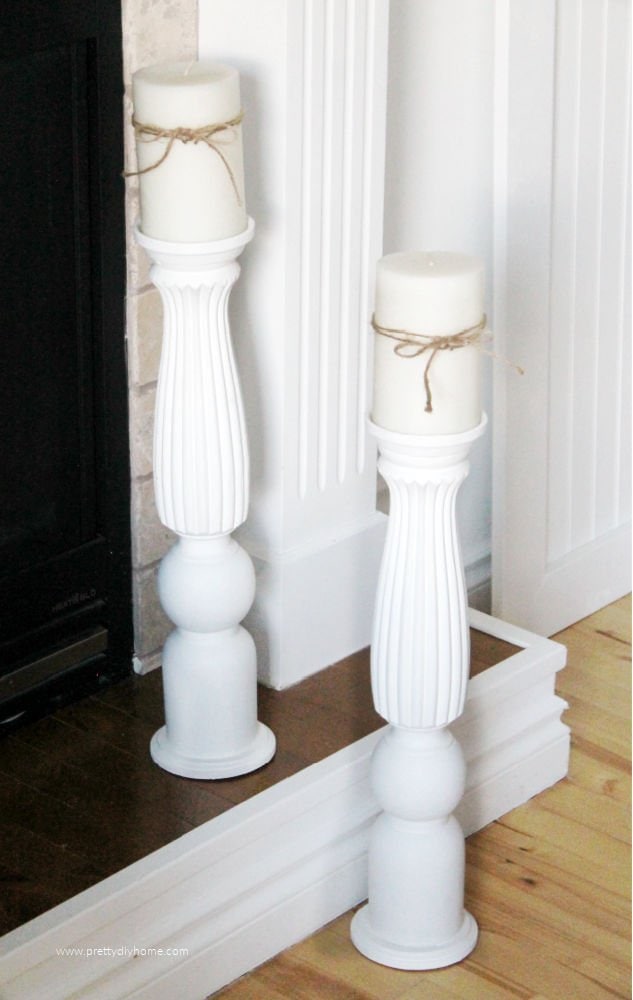 Two large floor sized candle holders in white sitting on a fireplace.