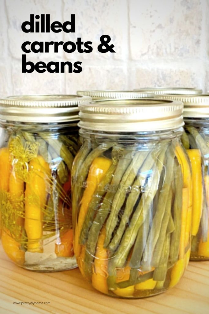 Jars of homemade dilled pickled carrots and beans, pretty in orange and green sitting on a kitchen counter.