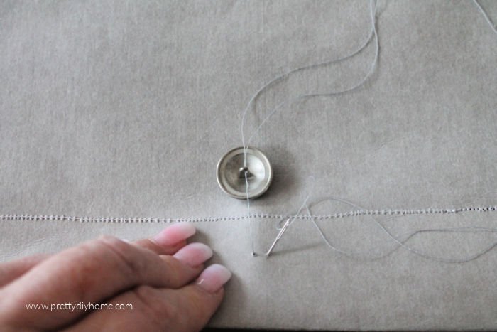 Sewing a button onto a DIY envelope cushion with a needle and thread.