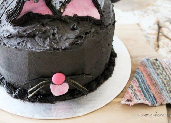 A closeup of Halloween cake with pink cat ears pink nose, licorice whiskers and a pink tongue.