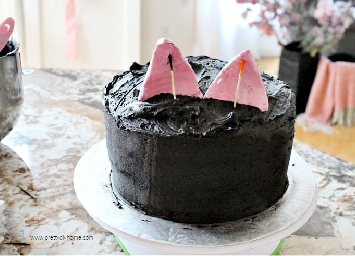 Placing pink fondant onto a Halloween cake to resemble cat ears.