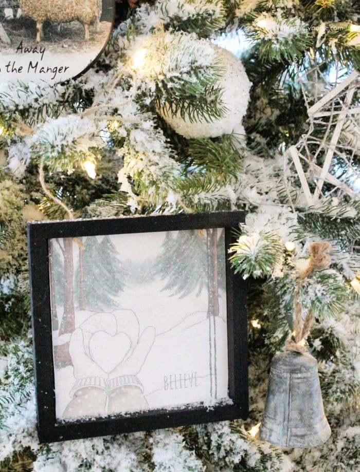 Soft looking Christmas tree ornaments in neutral colors with black frame hanging on a flocked Christmas tree.