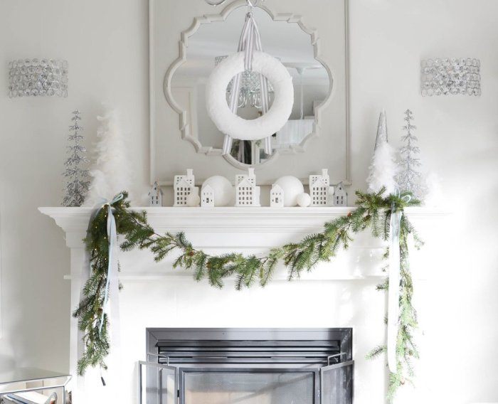 White Christmas decor decorated mantel with a white wreath mirror, white houses and candles.