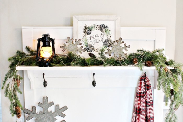 A farmhouse Christmas entry shelf decorated with galvanized snowflakes a lantern and merry Christmas sign.