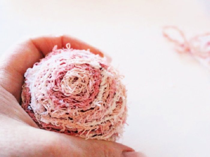 The underside of a DIY Christmas ornament in pink cotton thread, showing how to attach and start glueing the thread onto the Christmas ball ornament.using dollar tree supplies and cotton wool.