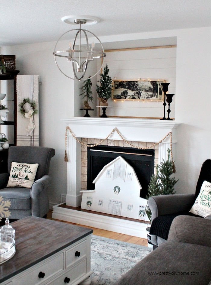 Living room decorated for Christmas in neutral farmhouse style including a Christmas mantel with large DIY barn