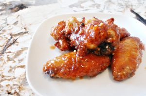 A small serving of oven roasted chicken wings, coated in a golden orange hot and sweet sauce.