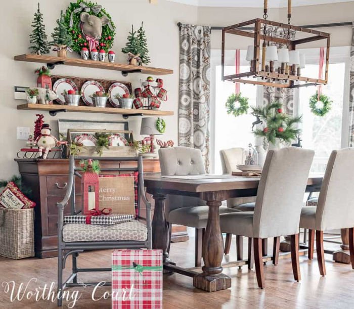 A farmhouse table and open shelves decorated in farmhouse Christas decorations, wreaths, faux Christmas trees, wreaths and red and white ribbon.