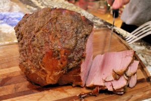 Sliced of oven baked ham with brown sugar apple glaze, being cut on a board before serving.