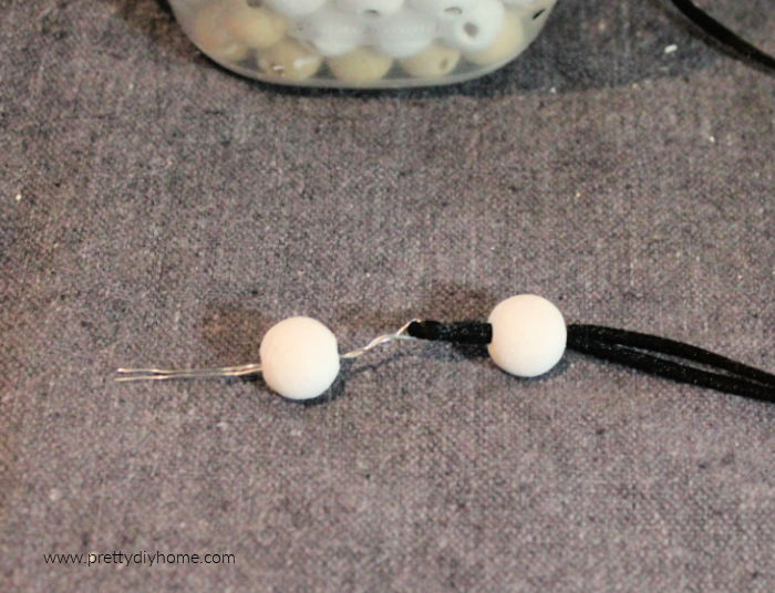 threading small white wood beads onto twine using wire.