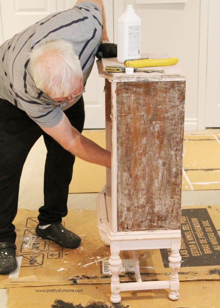 A man stripping blush coloured chalkpaint from a pink blush painted solid wood furniture.