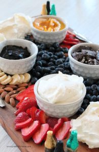 A pavlova charcuterie board with a palova recipe, strawberries, whipping cream, blackberries, blueberries, chocolate and fresh fruit.