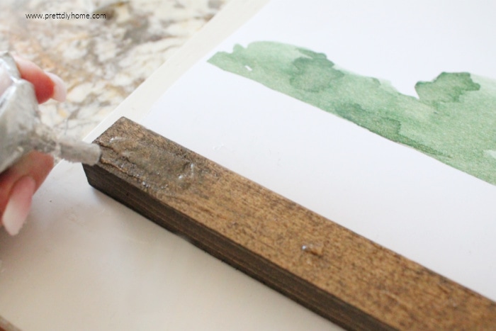 Adding glue to the back side of a wooden frame for making DIY farmhouse wall decor.