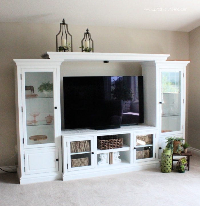 A painted entertainment center after picture. Its white with greenery and pink depression glass, and wicker baskets.