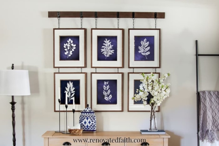 A hanging rail rack diy wall art idea. A wood strip is attached to the wall and then a collection of six different blue botanical prints hanging from it in frames.