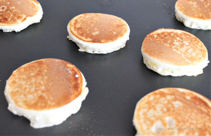 Mini golden brown lemon ricotta pancakes being cooked on a grill.