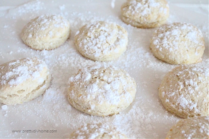 A baking tray full of light golden biscuits that are covered with a dusting of icing sugar.