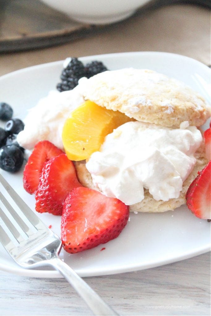 A serving of strawberry shortcake dessert thats been made with classic sweet biscuits. The strawberry shortcake is served with other berries and peaches as well as the strawberries.