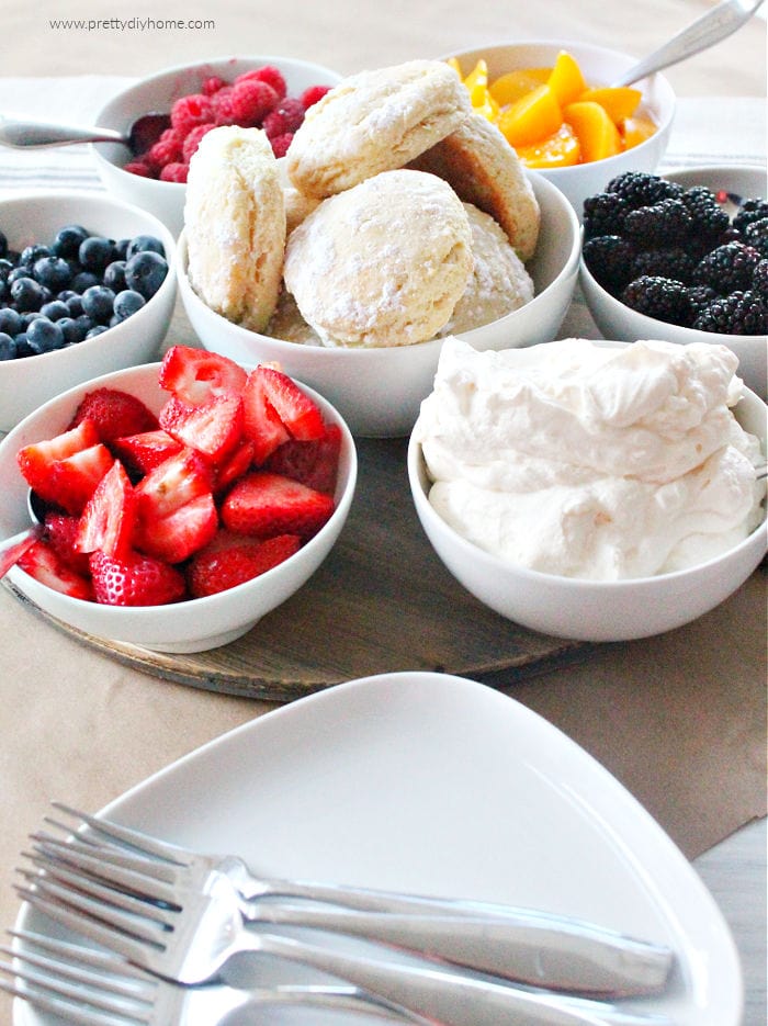 How to serve strawberry shortcake dessert charcuterie. Several small bowls with a dish of sweet biscuits in the middle surrounded by an assortment of fresh berries and whipping cream.