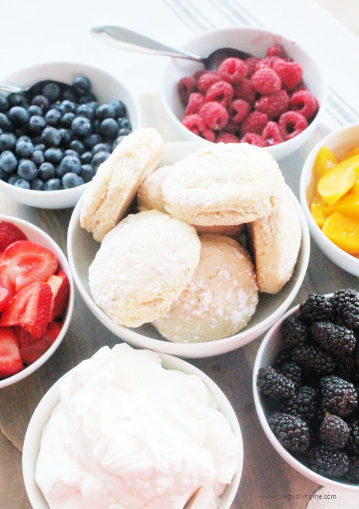 Strawberry Shortcake with sweet biscuits blackberries, raspberries, and whipping cream served in small bowls.