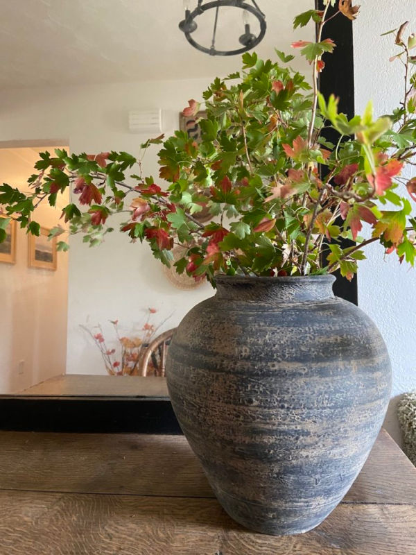 A large black and grey upcycled pottery vase holding a bouquet of orange and green leaves.