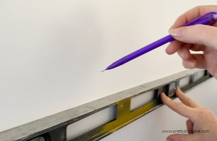 Using a level to mark shelf placement on the wall with a pencil