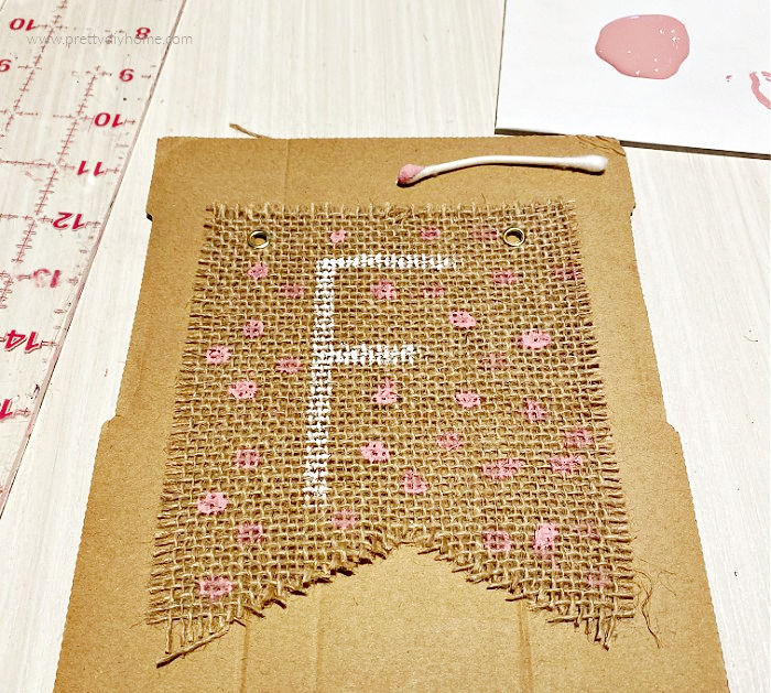 Pink Fall Banner with pink polka dots painted on Dollar Tree burlap banner kit. The letter F for the word Fall is painted on the front of the Fall bunting using white paint.