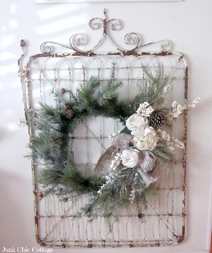 A white Christmas wall display with a vintage gate background behind a wreath and white decor.
