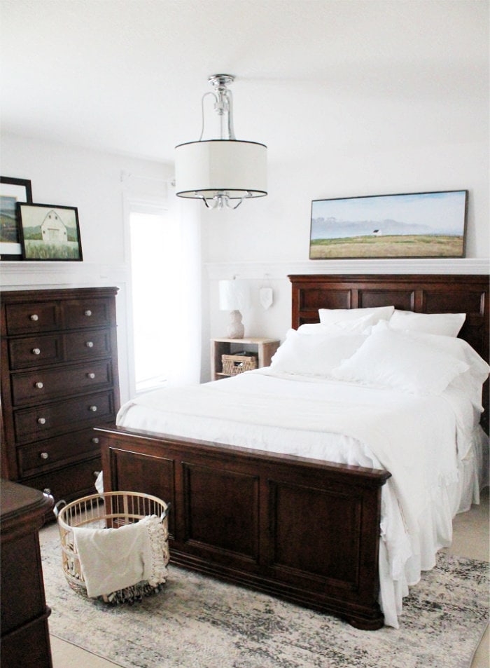 A refreshed master bedroom with DIY peg rails on the walls to hold pictures. There is white linene bedding and a vintage style bedroom furniture including a bleached wood night stand.