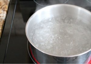 A large pot of pickle brine that is boiling on top of a stove. You can see lots of boiling bubbles.