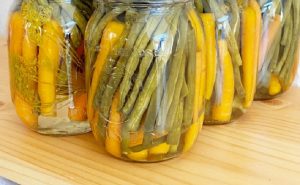 Pickled beans and pickled carrots lined up in a pattern inside of mason jars. There are five jars showing and the vegetables are layered inside mason jars.