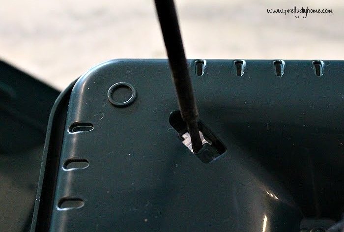 The bottom of a green plastic dollar store bird feeder, being pried open with a small screwdriver.