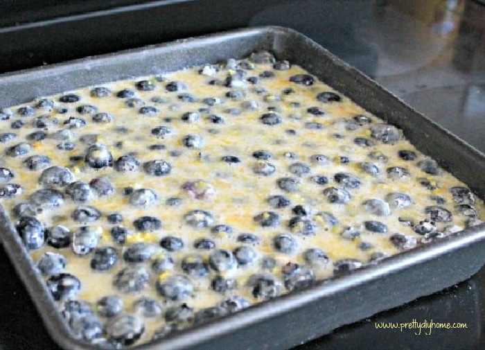 Fresh blueberries covered with lemon custard on top of a shortbread layer baking in a 9 by 9 inch pan.