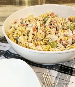 A large white pasta bowl filled with cold chicken pasta salad. The salad has rotini, cut up chicken,sausage, peppers, grapes, all drizzled with a creamy homemade dressing.