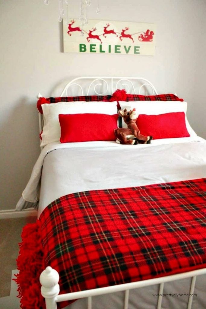 A double bed with a light grey cover, white pillows and a matching plaid fleece throw and pillow covers in red tartan plaid.