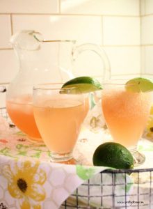 A large pitcher and two glasses of Vodka Slush, on a tray for serving. The vodka slush is pink grapefruit coloured and its served with a slice of lime.