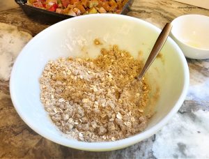 Mixing together rhubarb crisp recipe crumb coating. The crumb coating is a golden brown colour with flour, butter, brown sugar, oatmeal and cinnamon.