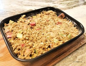 A rhubarb crisp recipe thats been baked. The rhubarb crisp is in a large black cereamic dish and is cooling on a cutting board.