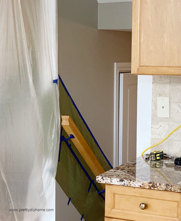 The rail to the downstairs of our home with a taped wall and doorway covered in plastic for staining.