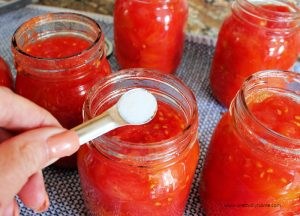 Adding a tsp of salt to a jar of canned tomatoes.