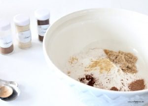 A large mixing bowl with cinnamon, nutmeg, and ginger spices, and the jars of spices sitting beside it.