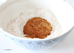 A large mixing bowl full of dry ingredients, with a center of wet pumpkin ingredients in the middle not mixed yet.