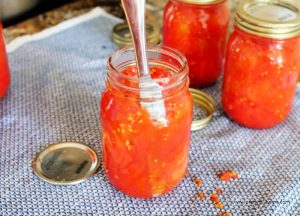 Packing jars with tomatoes using a knife.