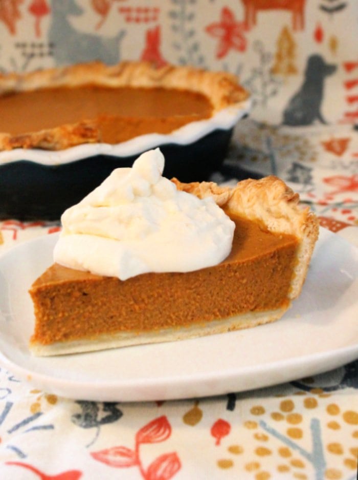 A large slice of pumpkin pie with whipped cream, sitting in front of a large pumpkin pie thats been made from scratch.