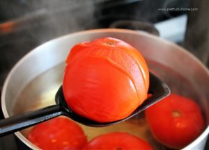 A tomato thats having the skin removed by boiling for canning. The tomato skin has split and it receding from the flesh of the tomato